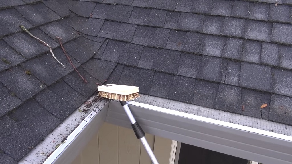 Using a long-handled brush to maintain gutter guards