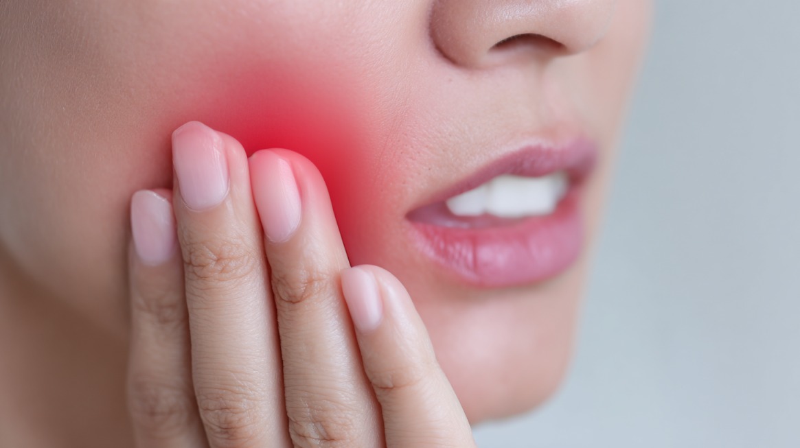 Close-up of a woman touching her cheek with a red area highlighting severe dental pain