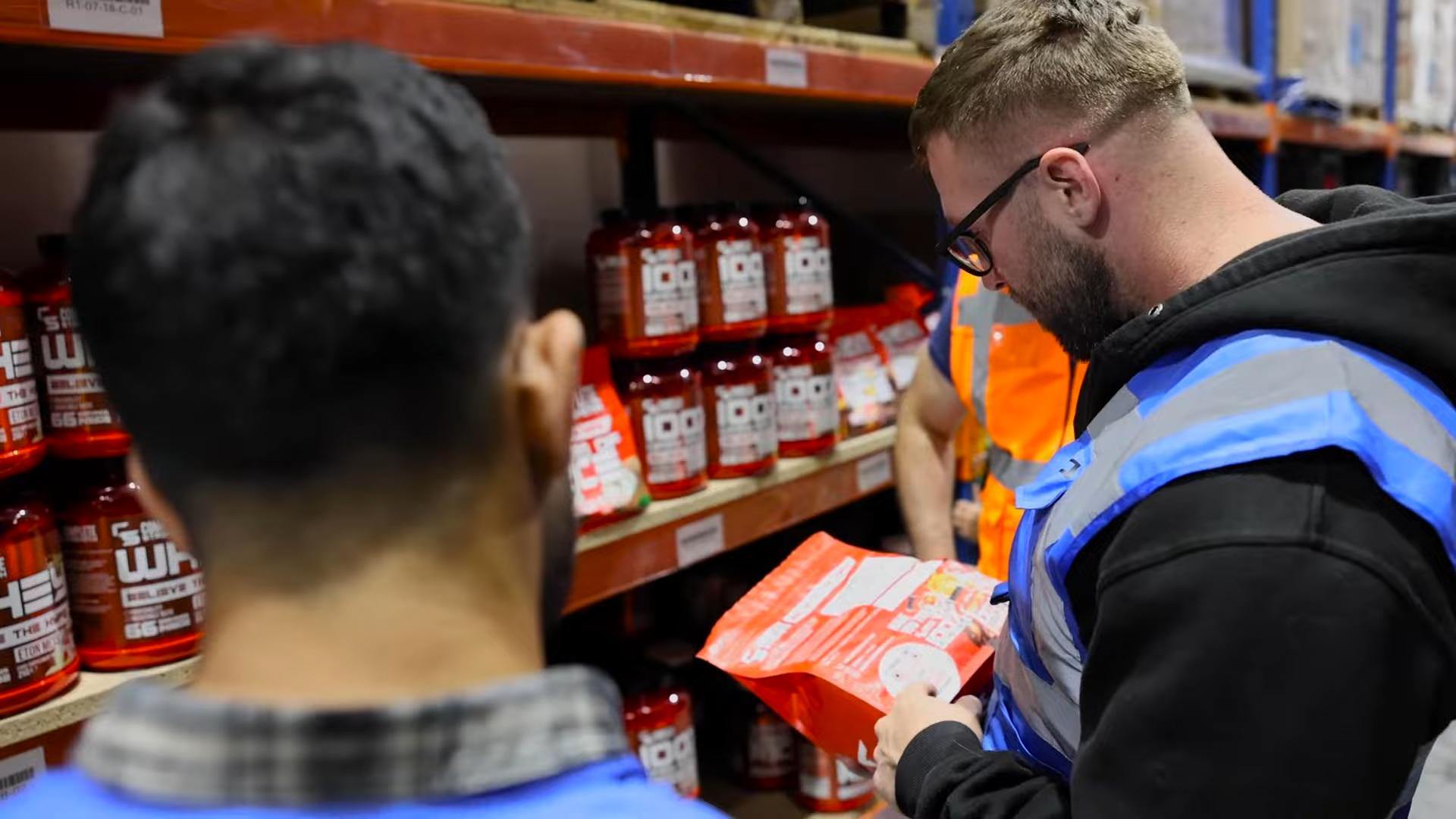 Two warehouse workers inspecting packaged products on storage shelves.
