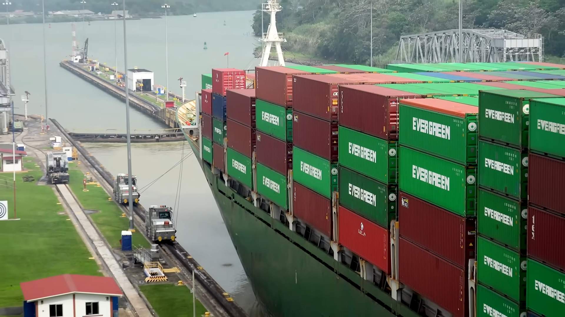 Large cargo ship carrying stacked containers through a canal lock.