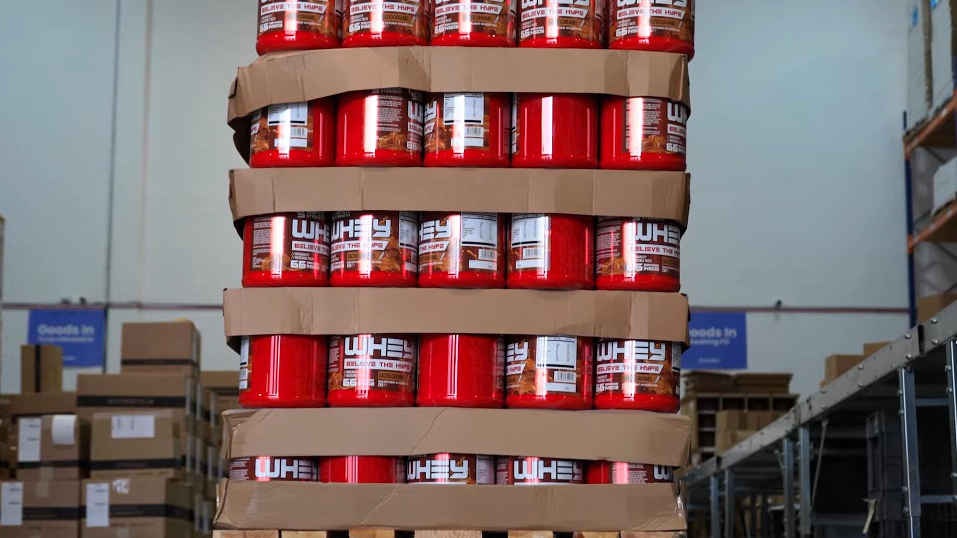 Red supplement containers stacked in cardboard trays inside a warehouse.