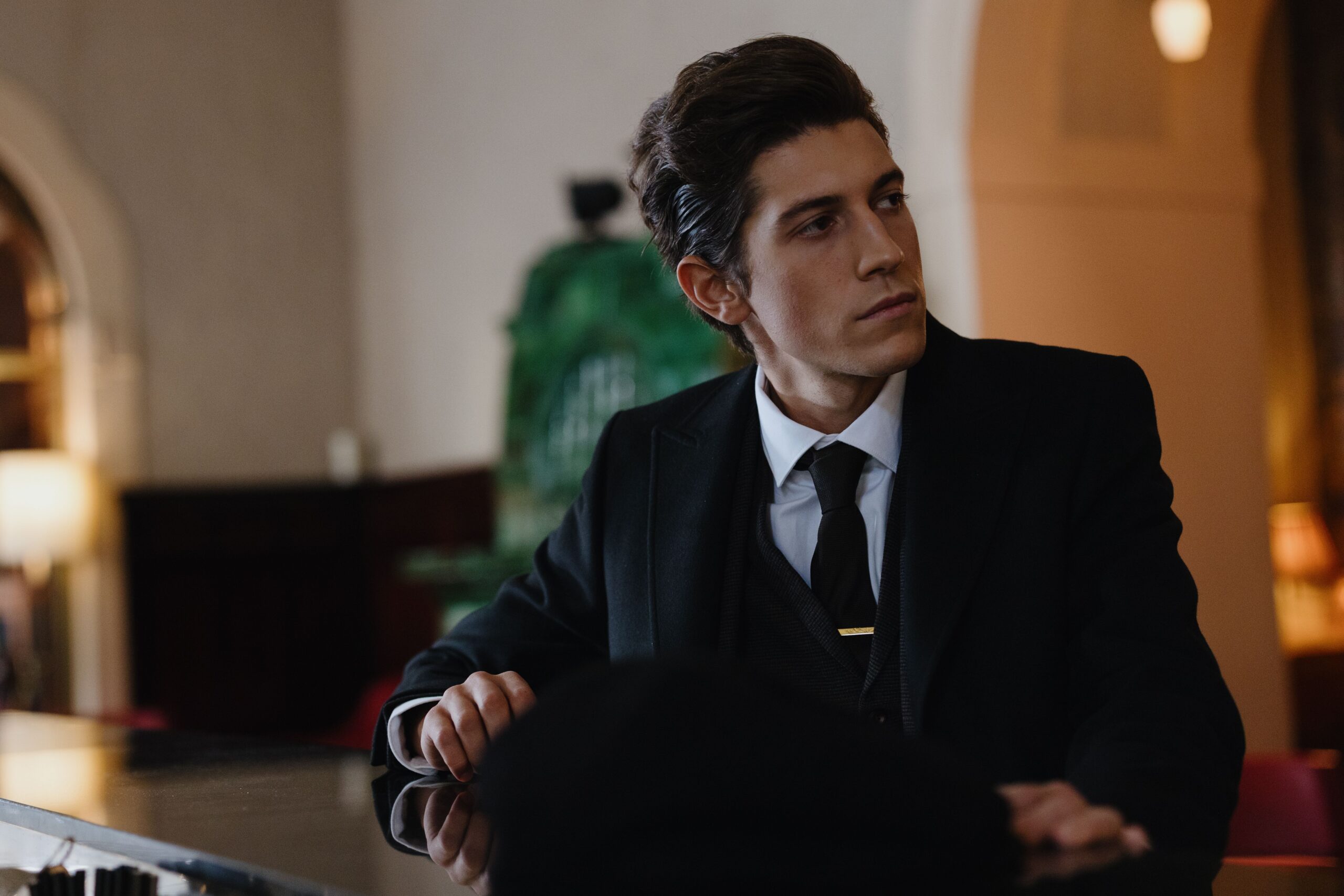 Stylish man in a black suit seated indoors, exuding sophistication