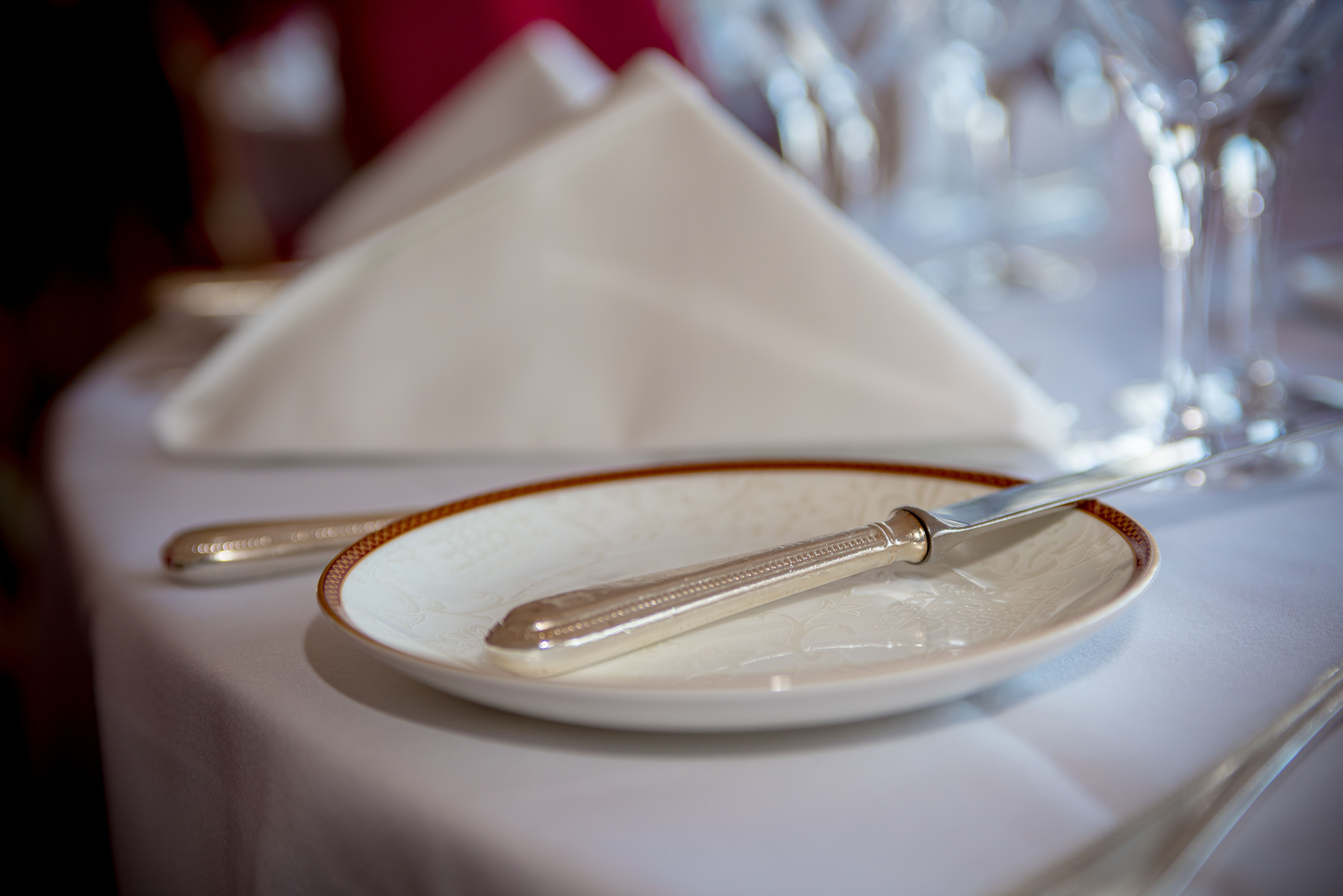 Close-up of a formal table setting with silverware, a plate, and a folded napkin on a white tablecloth