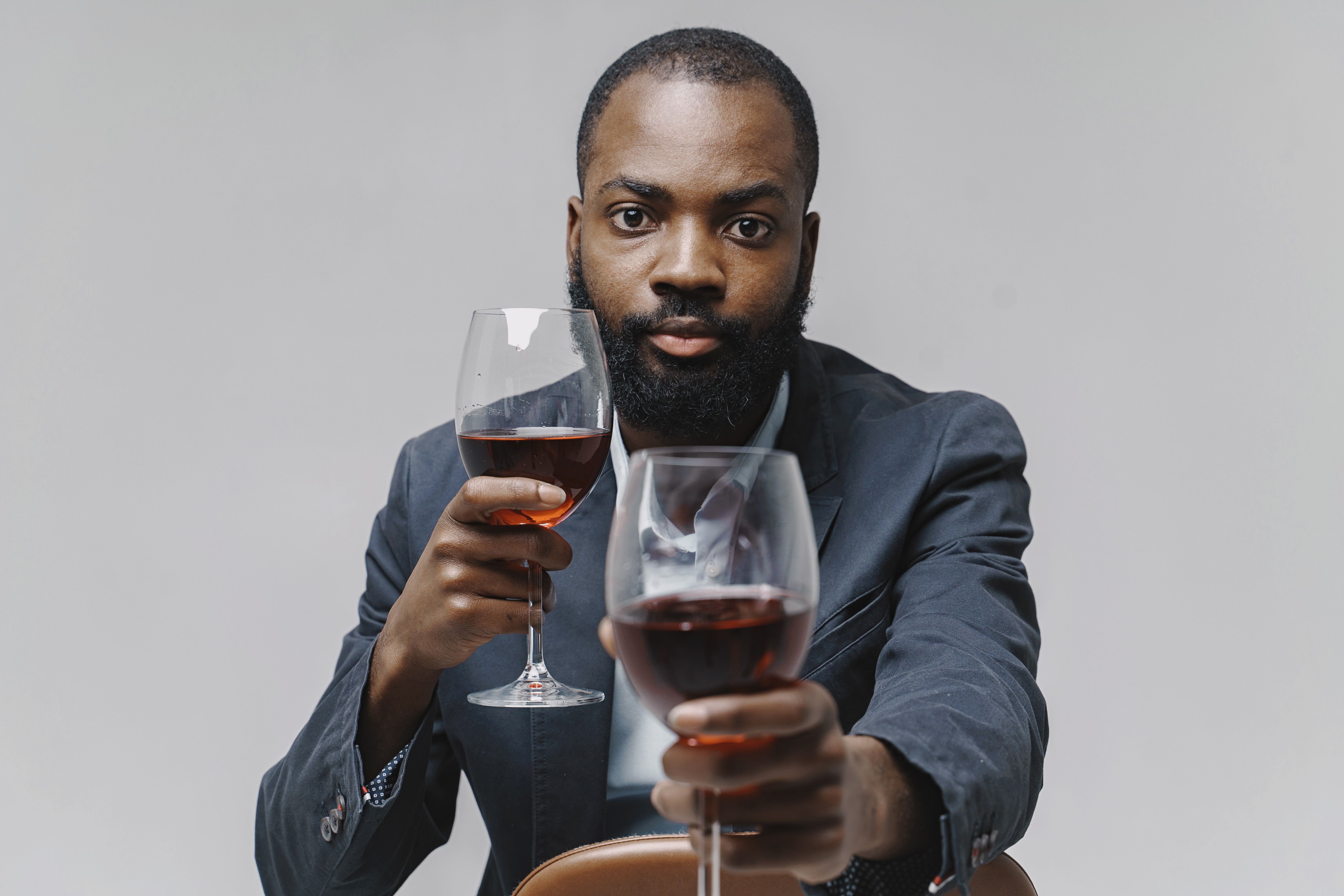 A well-dressed man holding two wine glasses in a studio setting